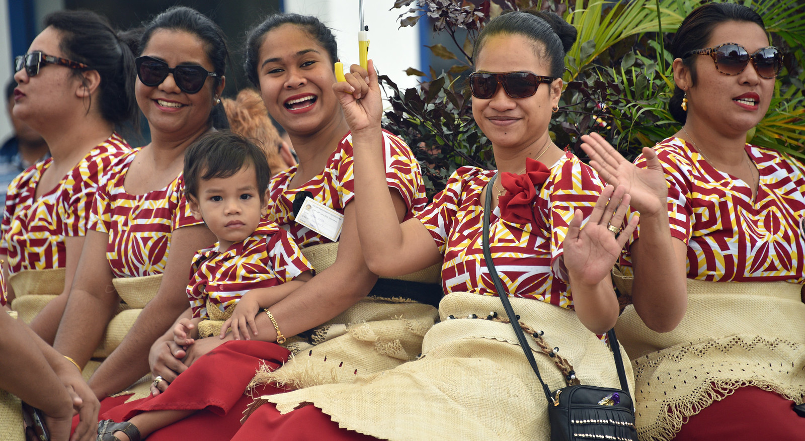 A joyful gathering of Tongan women and children waving at the camera, showcasing the warmth and hospitality of island life.